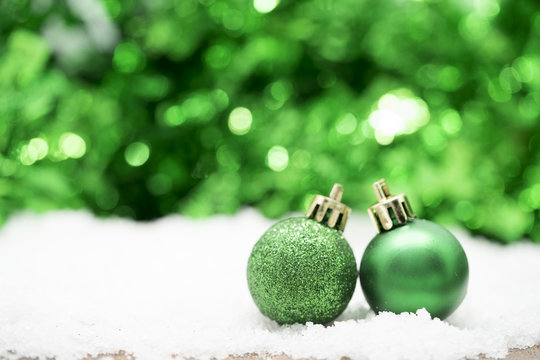 Green Christmas balls on snow against green bokeh background