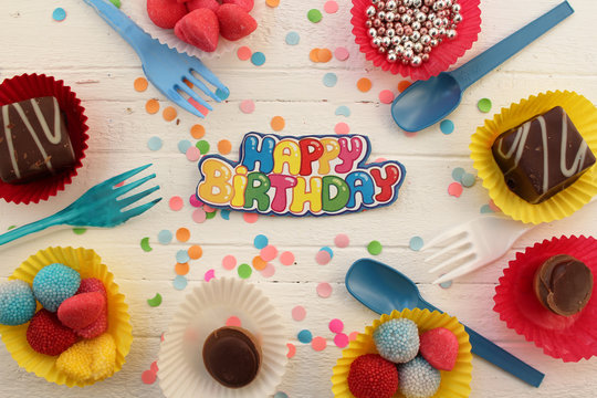 Birthday celebration cupcake, candy, plastic fork and spoon and confetti background 