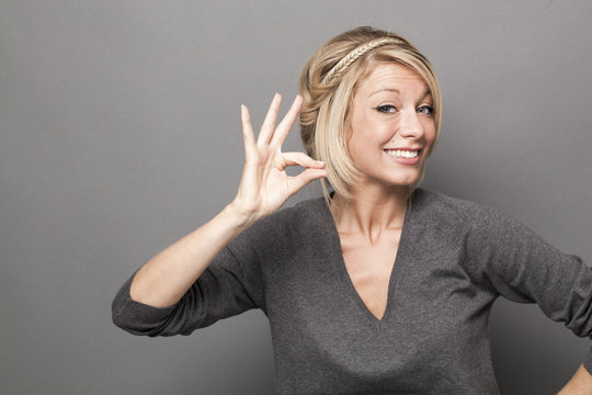 body language concept - smiling 20s blond woman making the sign of a tiny, small product with her hands,studio shot on gray background