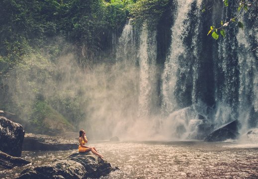 Beautiful woman sitting near waterfall enjoying the sun, Phnom Koulen at Siem Reap, Cambodia