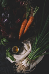 Green onions, carrots, beets and rosemary on textiles on a black wooden background top view