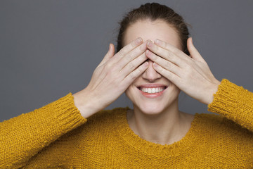 glowing happiness concept - playful 20s girl smiling in playing hide-and-seek for joy and...
