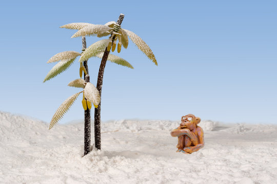 sad clay monkey sitting in the snow near the snow-covered bananas palms