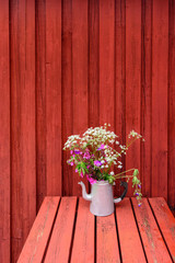 Norwegian beautiful wildflowers in watering can on the red wooden background