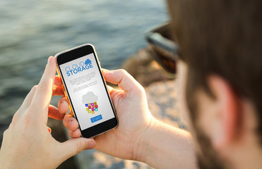 Man using his  mobile phone on the coast with cloud storage on t