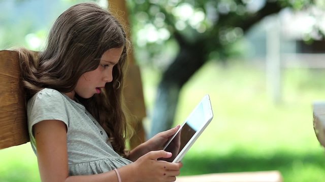 Nice girl playing the game on Tablet PC. Nice girl with Tablet-PC sits on the bench. True sincere emotions. Beautiful girl with tablet computer sits on the bench
