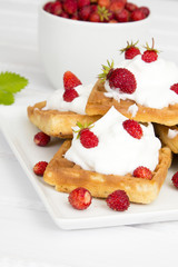 waffles with wild strawberries and whipped cream on white table