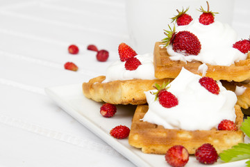 waffles with wild strawberries and whipped cream on white table