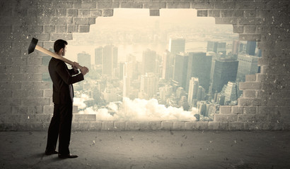 Business man hitting wall with hammer on city view