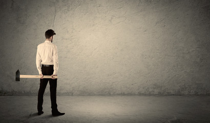 Business man standing in front of a grungy wall with a hammer