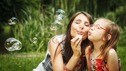 Mother and little girl blowing soap bubbles in park.