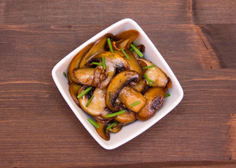 Baked mushrooms on square bowl on wooden table seen from above