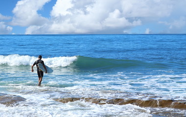 Surfer in black wet suit walking in to water on sunny day