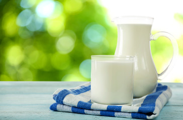 Pitcher and glass of milk on bright background