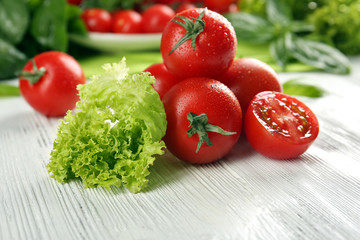 Cherry tomatoes with basil and lettuce on wooden table close up