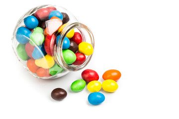 Transparent glass jar with colorful chocolate candies on white b