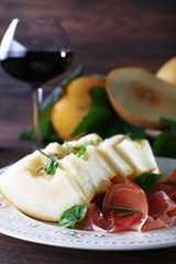 Melon with prosciutto of Parma ham on wooden table, closeup