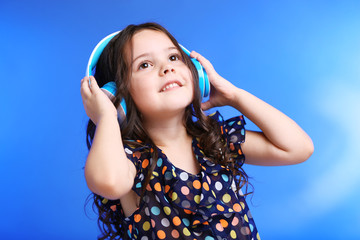 Happy little girl in colourful shirt with headphones on blue background