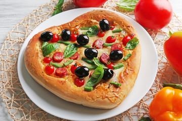 Delicious heart shaped pizza on the plate with vegetables around, close up