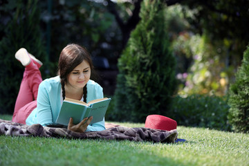 Young woman with book lying on green grass outdoors