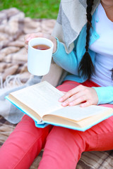 Young woman with book sitting on green grass outdoors