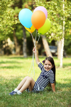 Happy little girl in striped dress with colourful balloons in the park