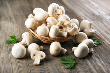 Champignon mushrooms in a basket and parsley on grey wooden background