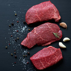 Top view of raw marbled beef steaks on a black wooden background
