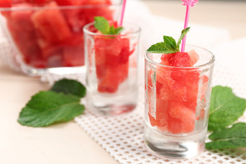 Cold watermelon pieces in glasses, on wooden table background