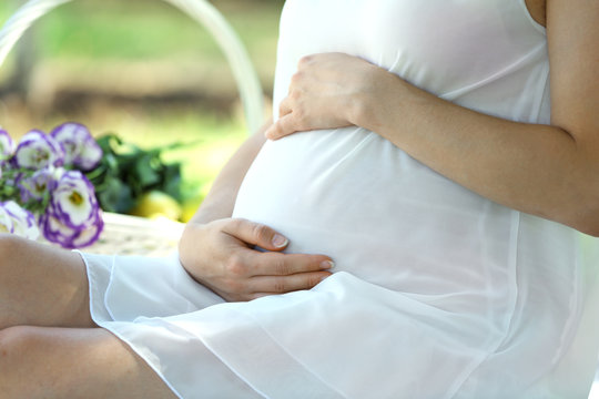 Attractive pregnant woman on white blanket in the park, close up