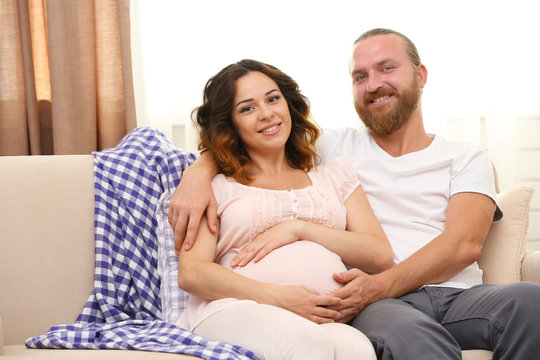Happy beloved couple in waiting for baby's birth on sofa in the room