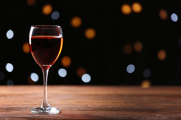 Wine glass on wooden table against defocused lights background