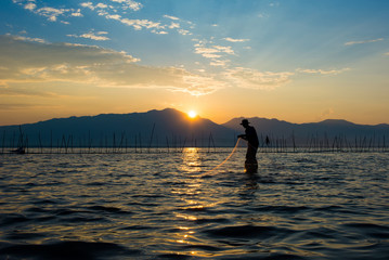 Silhouettes of the traditional fishermen throwing fishing net du