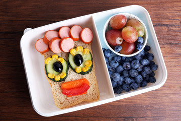 Creative sandwich with fruits in lunchbox on wooden background