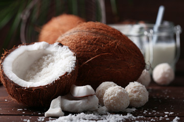 Candies in coconut flakes, glass of milk and fresh coconut on dark wooden background