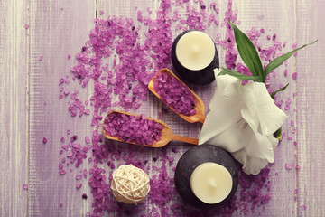Spa composition of candles, stones, sea salt and flower on purple wooden background
