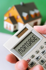 family house and  hand holding a pocket calculator with Mortgage