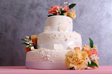 White wedding cake decorated with flowers on  pink wooden table against grey background