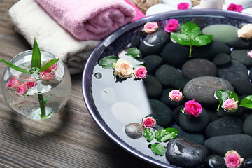 Spa composition of candles, flowers and stones in water, on wooden background