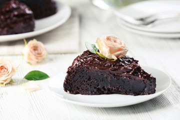 Piece of chocolate cake decorated with flowers on white wooden table