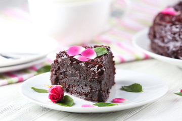 Piece of chocolate cake decorated with flowers on white wooden table