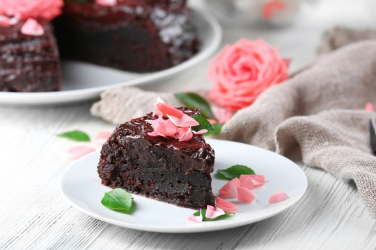 Piece of chocolate cake decorated with flowers on white wooden table