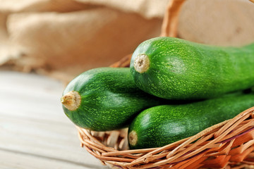Fresh zucchini in wicker basket on wooden background
