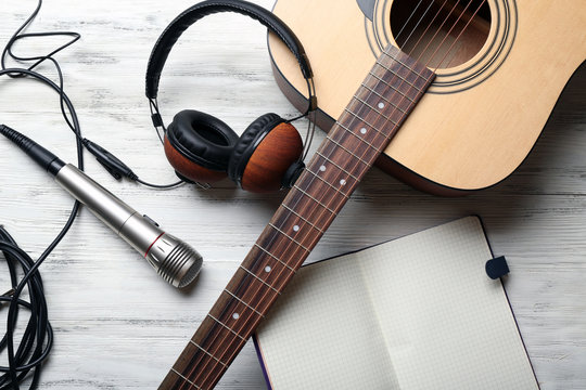 Acoustic guitar, headphones, opened notebook and microphone on wooden background, close up