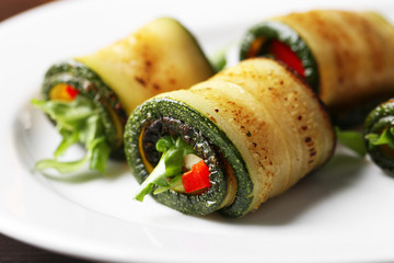 Zucchini rolls with cheese, bell peppers and arugula on plate, close-up