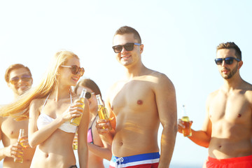 Happy young friends drinking beer at the beach, on sky background