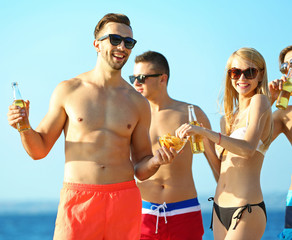 Happy young friends drinking beer at the beach, on sky background