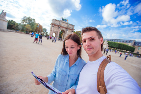 Romantic young couple with map of city taking selfie background famous Louvre in Paris