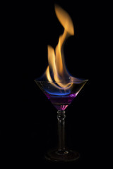 Martini glass with purple drink is on fire and very hot