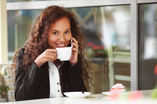 Young smiling woman speaking by cellphone and drinking coffee at the restaurant's terrace